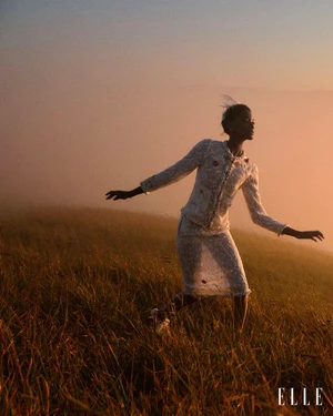 Model in a white textured skirt suit stepping gracefully across a misty grassy hillside at sunrise.
