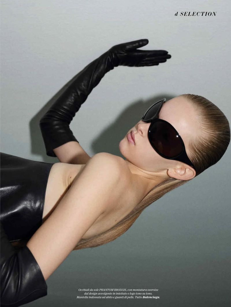 Model Amelie Loblich wearing oversized black sunglasses and long black leather gloves against a grey studio backdrop.