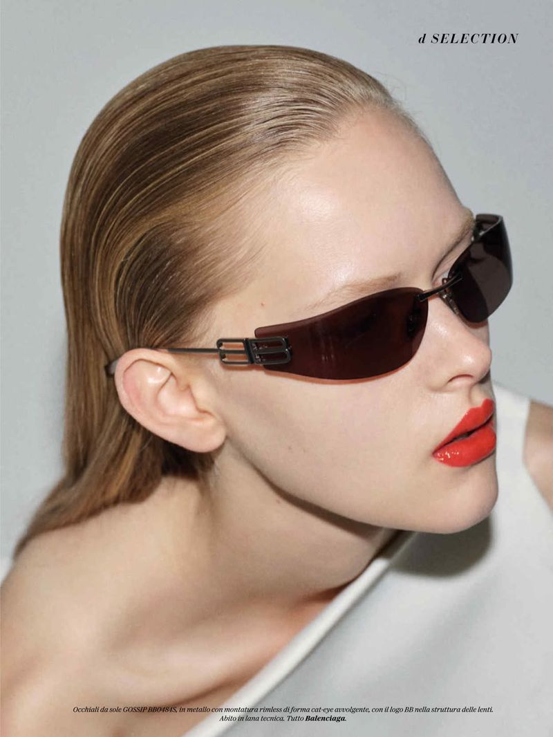 Amelie Loblich wearing dark wraparound sunglasses with red lipstick and slicked-back hair against a neutral studio backdrop.
