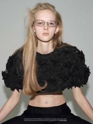 Model Amelie Loblich wearing rectangular wire-rim glasses and a black floral textured crop top against a pale grey background.