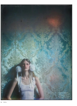 Model wearing white tank top with large fluffy white hair pompons against patterned teal wall for Telva magazine