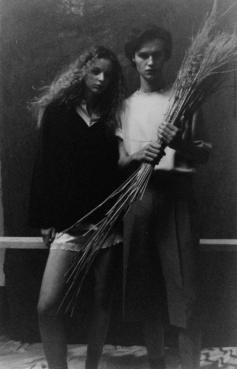 Monochrome portrait of a woman and man standing together in studio, the man holding a bundle of dried wheat stalks.