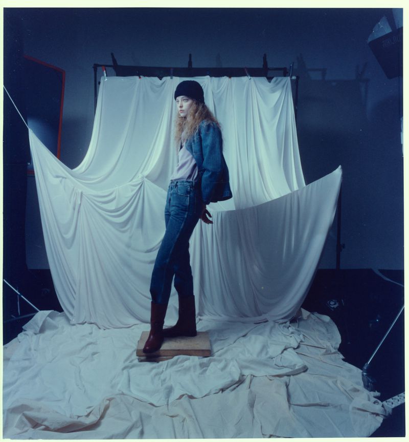 Model Boy Dijkhuis posing on a wooden block in front of draped fabric backdrop wearing denim jeans and a black beanie.