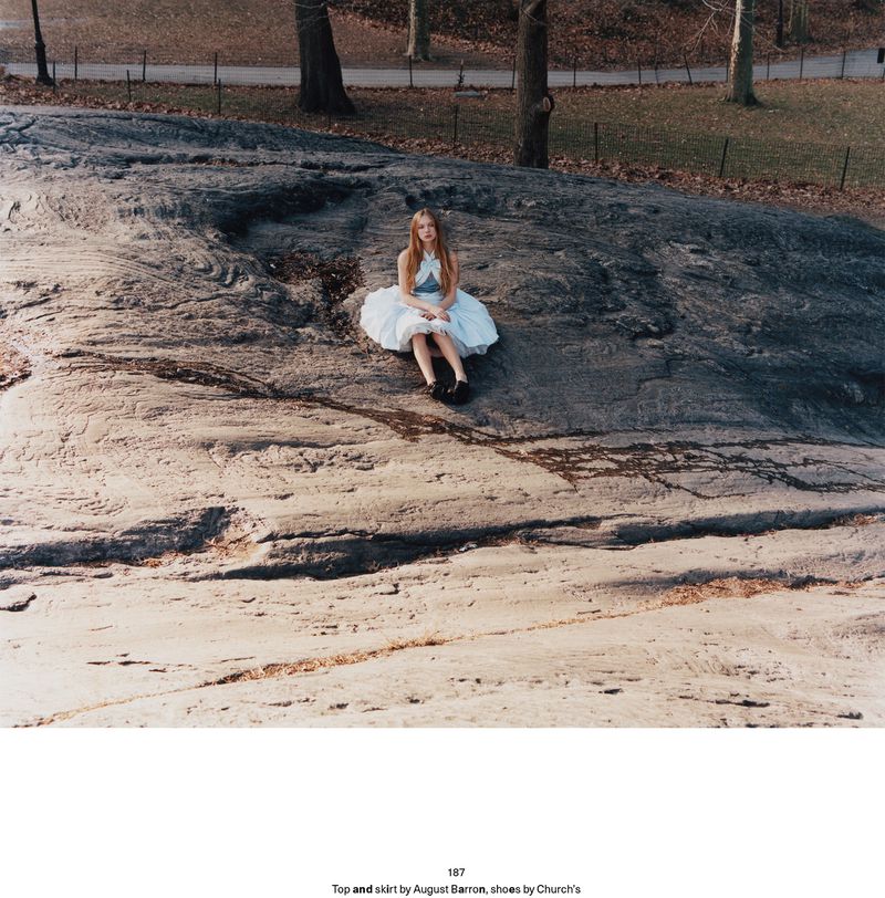 Model Secret Snow seated on a large dark rock wearing a white flared dress in a park setting for Middle Plane Magazine.