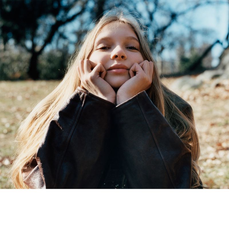 Model Secret Snow resting her chin in her hands wearing a dark leather jacket outdoors in a close-up portrait.