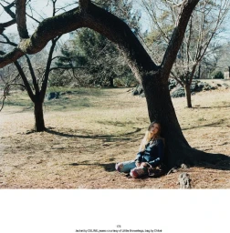 Model leaning against a large tree trunk in a park setting for Middle Plane Magazine editorial Secrets Out