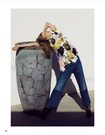 Model Clara Heitkamp leans against a large textured urn wearing a floral applique top and two-tone denim jeans in bright sunlight.
