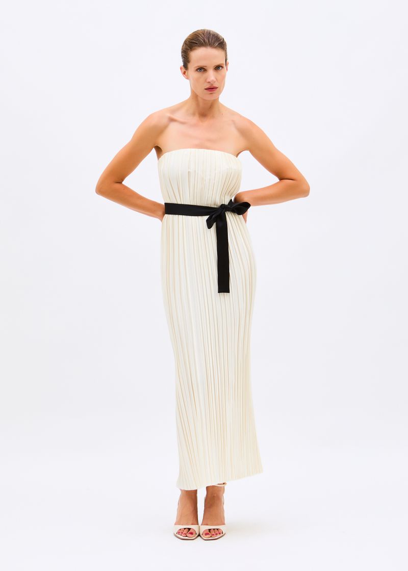Model Fanny Francois in an off-white strapless pleated column dress with a black sash against a white background.