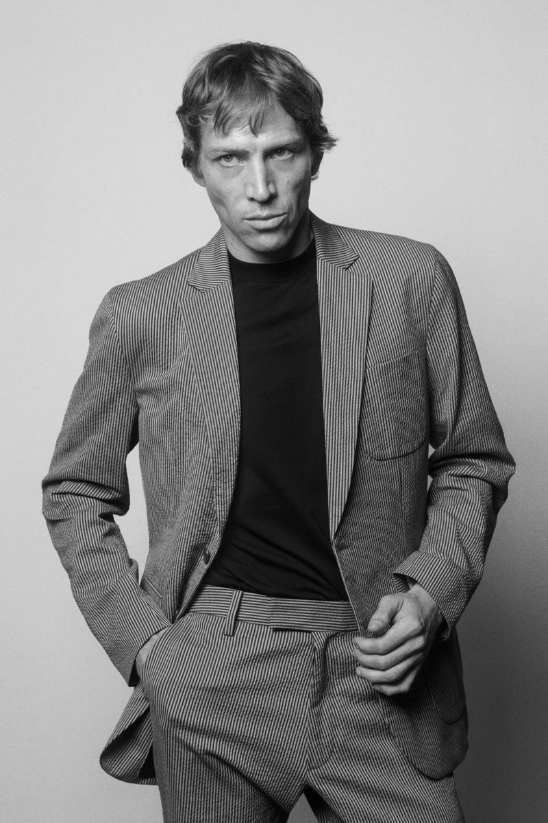Model Mike Vasilakis wearing a textured tailored suit and dark crewneck in a black and white studio portrait for Rag & Bone.