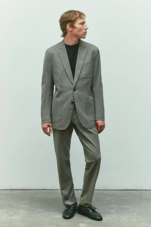 Model Mike Vasilakis wearing a grey tailored suit and black crewneck shirt against a neutral studio backdrop for Rag & Bone menswear.