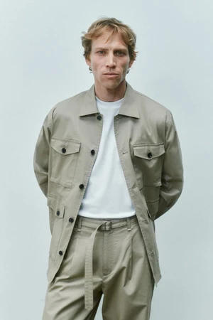 Model Mike Vasilakis in a beige utility jacket, white t-shirt, and matching trousers for Rag & Bone menswear.