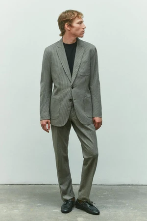 Model Mike Vasilakis wearing a grey tailored suit and black crewneck shirt against a neutral studio backdrop for Rag & Bone menswear.