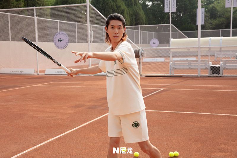 An adult male stands on a tennis court in a sporty outfit, ready to hit a tennis ball with a racket during daytime.