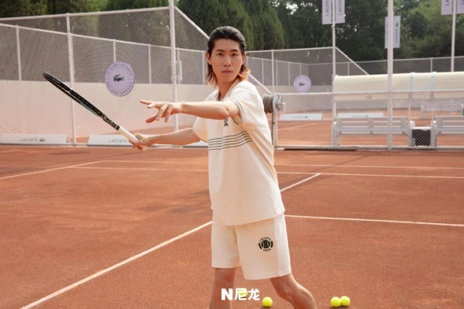 An adult male stands on a tennis court in a sporty outfit, ready to hit a tennis ball with a racket during daytime.