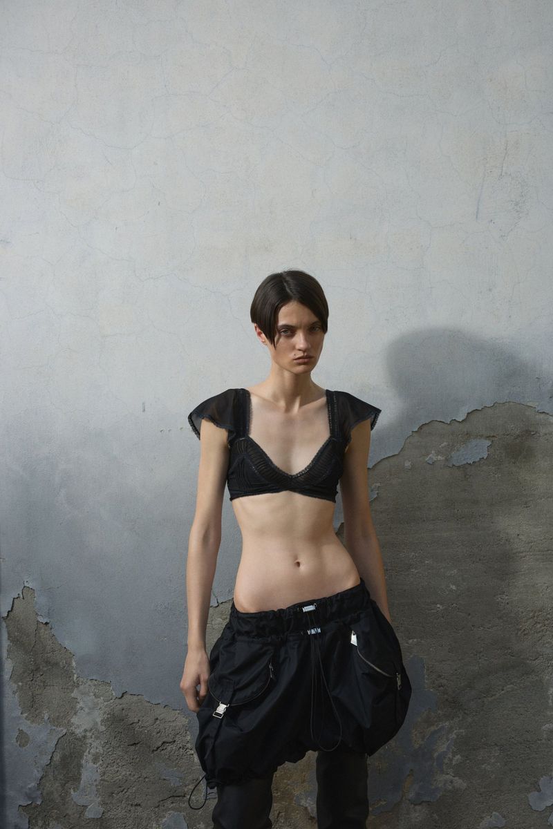 Model Tanya Churbanova wears a black ruffled bralette and voluminous low-rise cargo shorts against a distressed concrete wall.