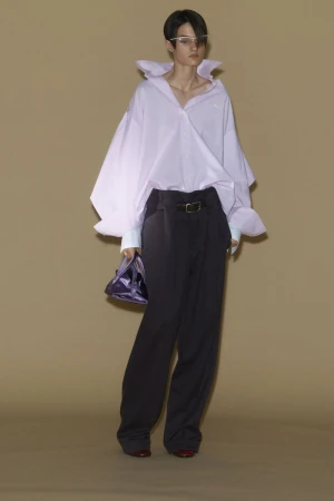 Model Tanya Churbanova posing in an oversized light pink collared shirt and black wide-leg trousers with a purple handbag.