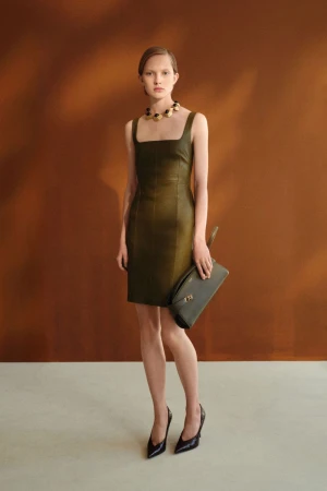 Model wearing an olive green sleeveless leather mini dress, chunky necklace, and black heels, holding a matching green clutch.