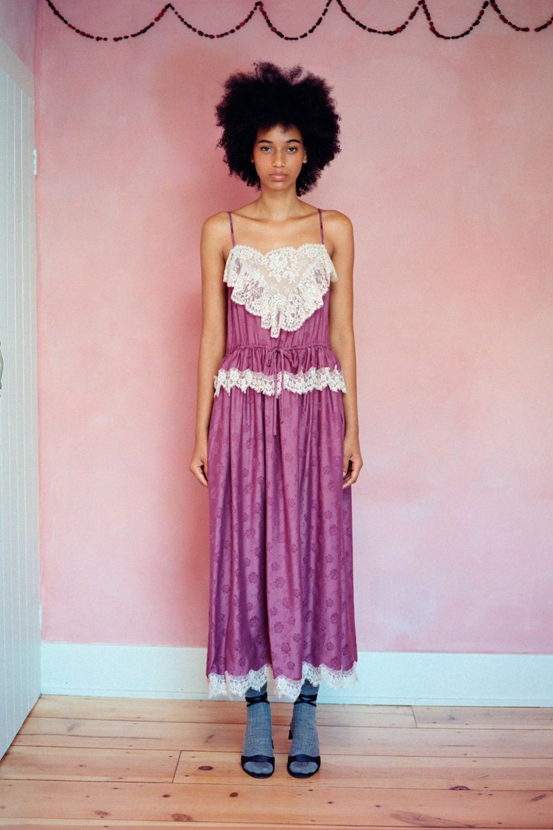 Model wearing a mauve lace-trimmed slip dress with grey socks and sandals against a soft pink wall.