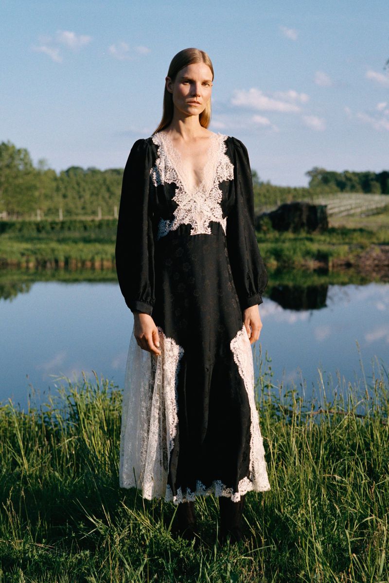 Model Suvi Riggs wearing a long black puff-sleeve dress with white lace trim by a pond in the Sea RS27 lookbook.