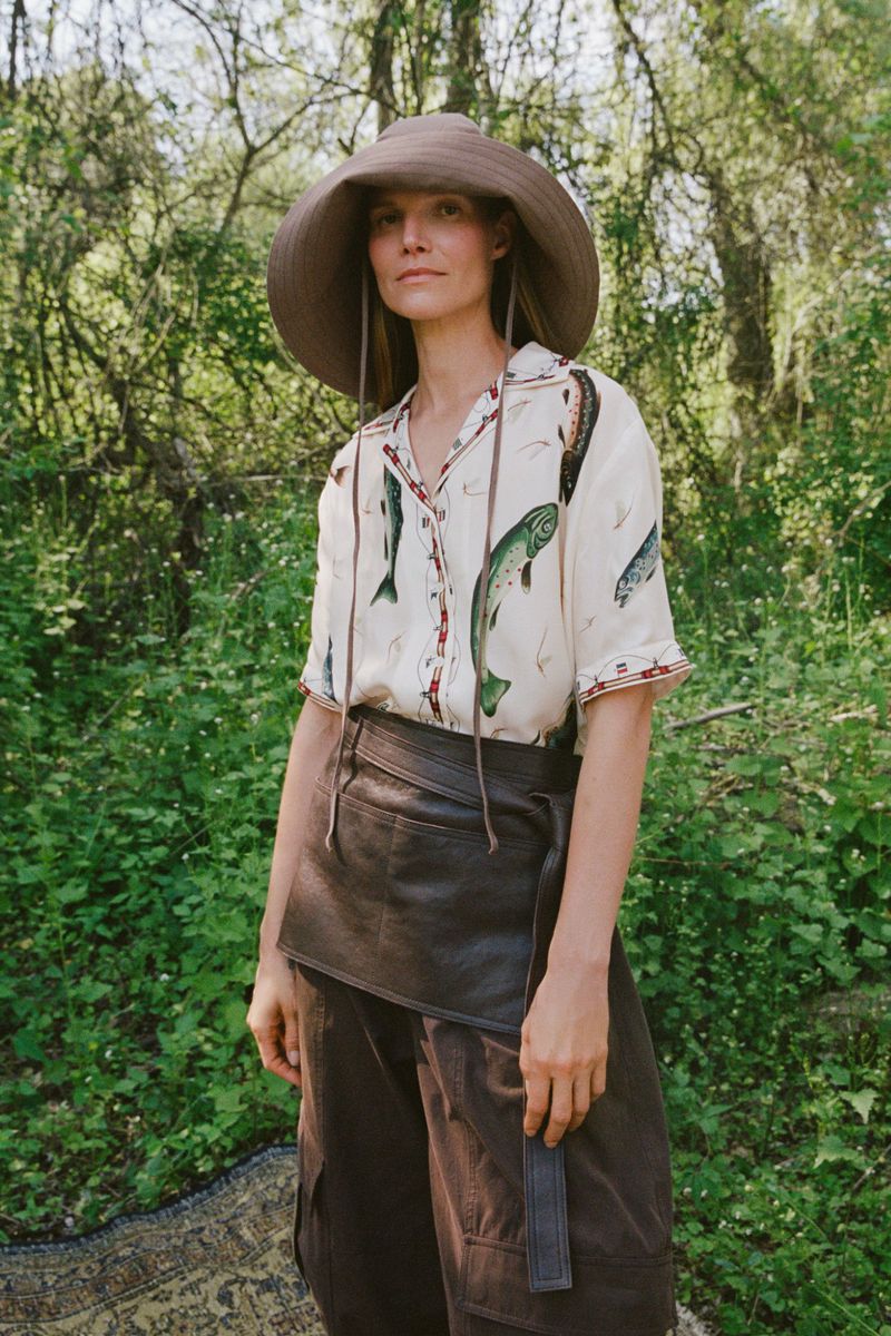 Suvi Riggs wearing a wide-brim brown hat, fish print shirt, and leather apron outdoors.