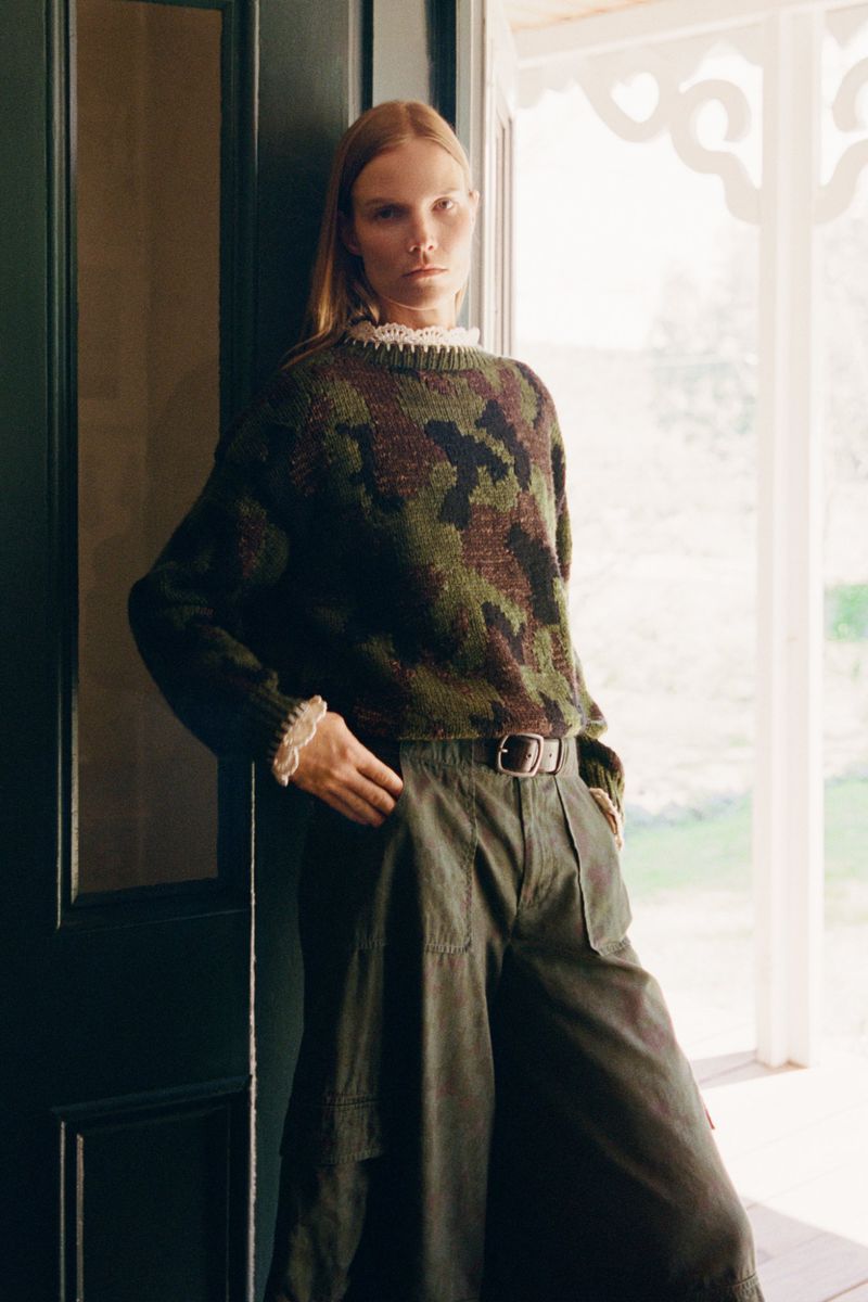 Model Suvi Riggs wearing a green camouflage knit sweater and wide-leg trousers in a doorway for Sea RS27 Lookbook.