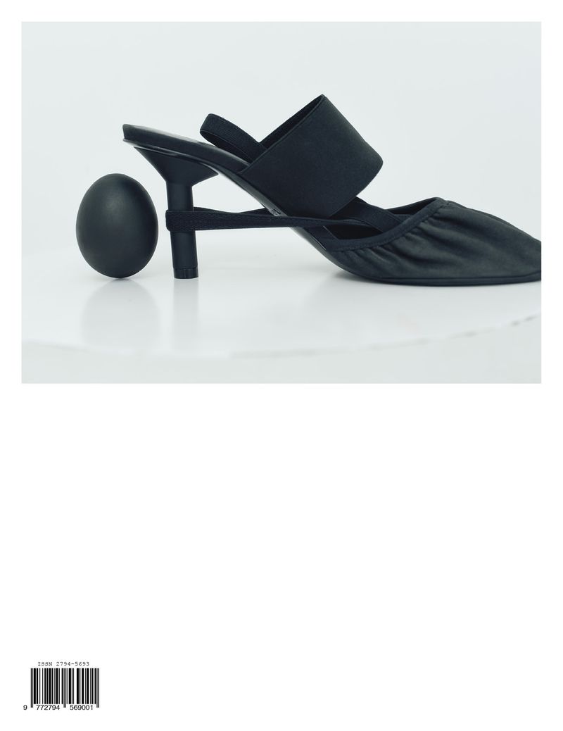 Black kitten heel shoe and black egg on a white reflective surface, showcasing footwear and minimalistic still life photography.