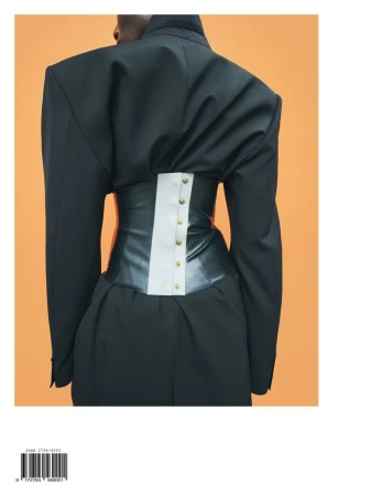 Back view of a person wearing an oversized black tailored jacket cinched with a dark leather corset against an orange backdrop.