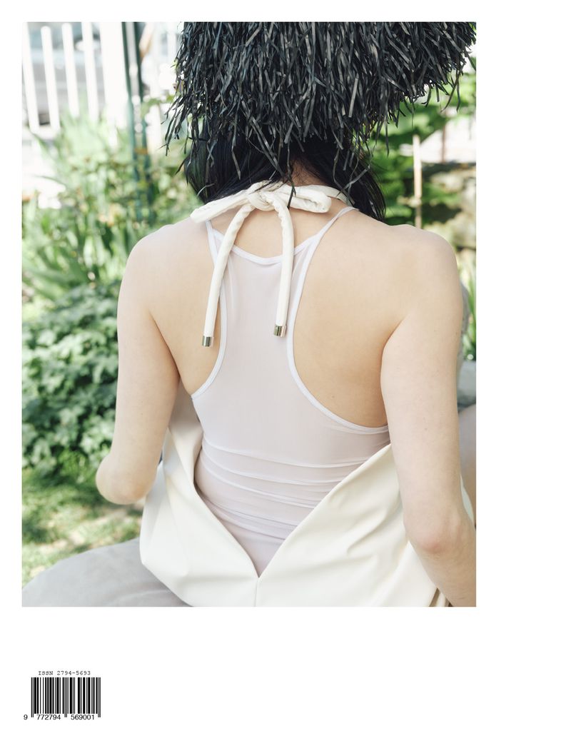 Back view of a woman with a white halter top and feathered headpiece outdoors, creating a fashion-forward and artistic composition.