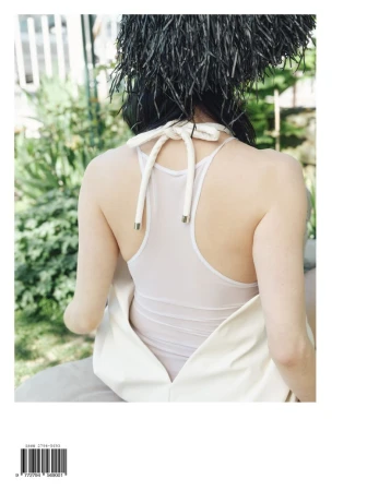Back view of a woman with a white halter top and feathered headpiece outdoors, creating a fashion-forward and artistic composition.