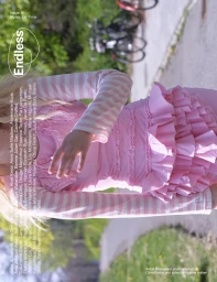 Model wearing a pink ruffled dress and striped sleeves outdoors on an asphalt path near blurred greenery.