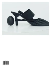 A black pointed low-heel mule shoe balancing beside a matte black egg on a plain white surface.
