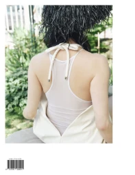 Model seen from behind wearing a white halter top and textured black hat against a garden background.