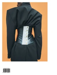 Back view of a person wearing an oversized black tailored jacket cinched with a dark leather corset against an orange backdrop.