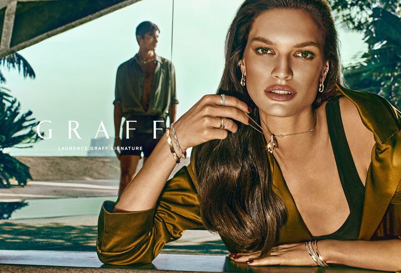 Model Faretta poses wearing Graff diamond jewelry and an olive satin jacket, with Akbar Shamji in the background.