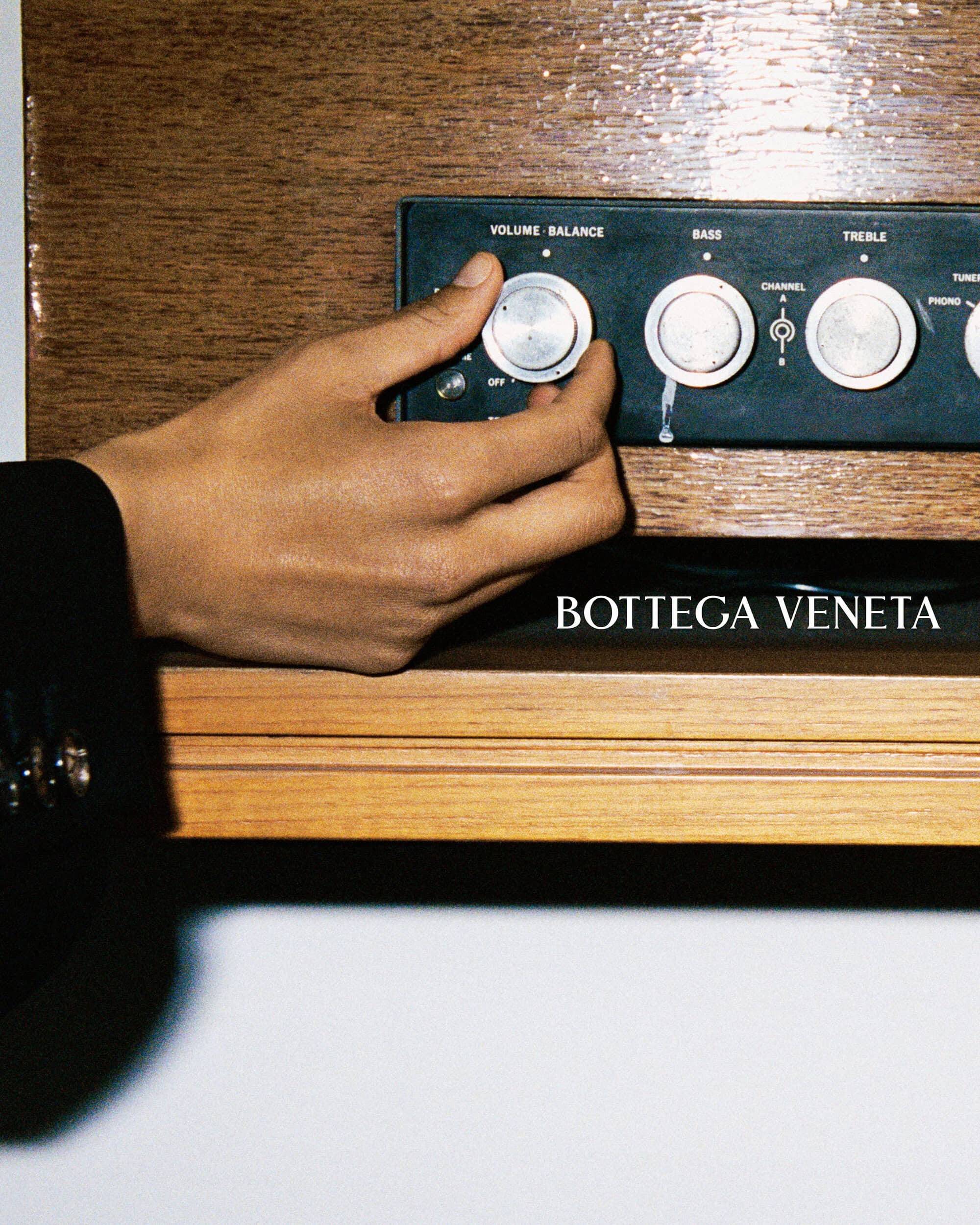 A hand wearing a black blazer sleeve adjusts a silver volume knob on a vintage wooden stereo receiver.