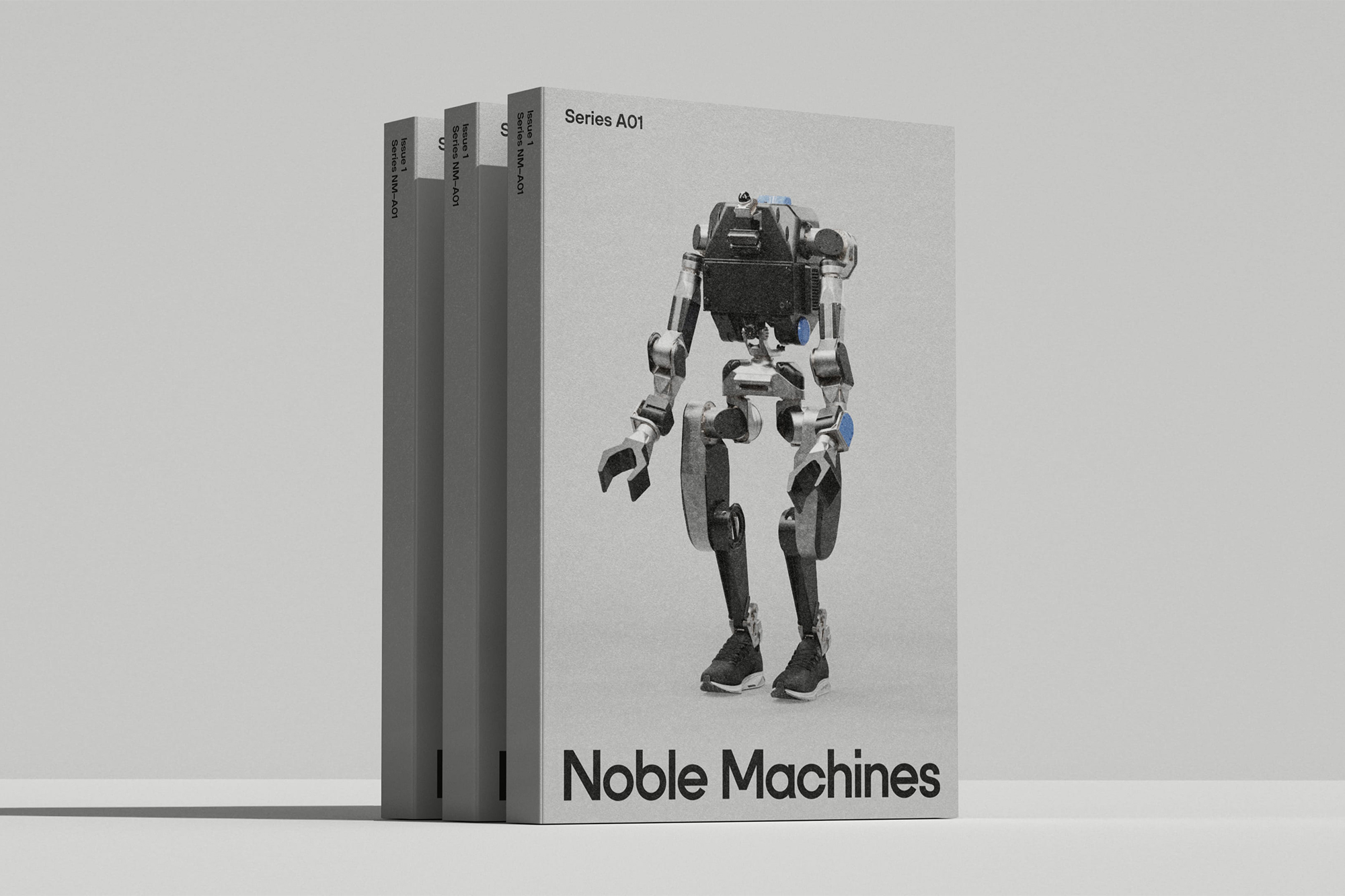 Three grey Noble Machines Series A01 brand identity books featuring a bipedal robot graphic standing on a seamless grey studio surface.