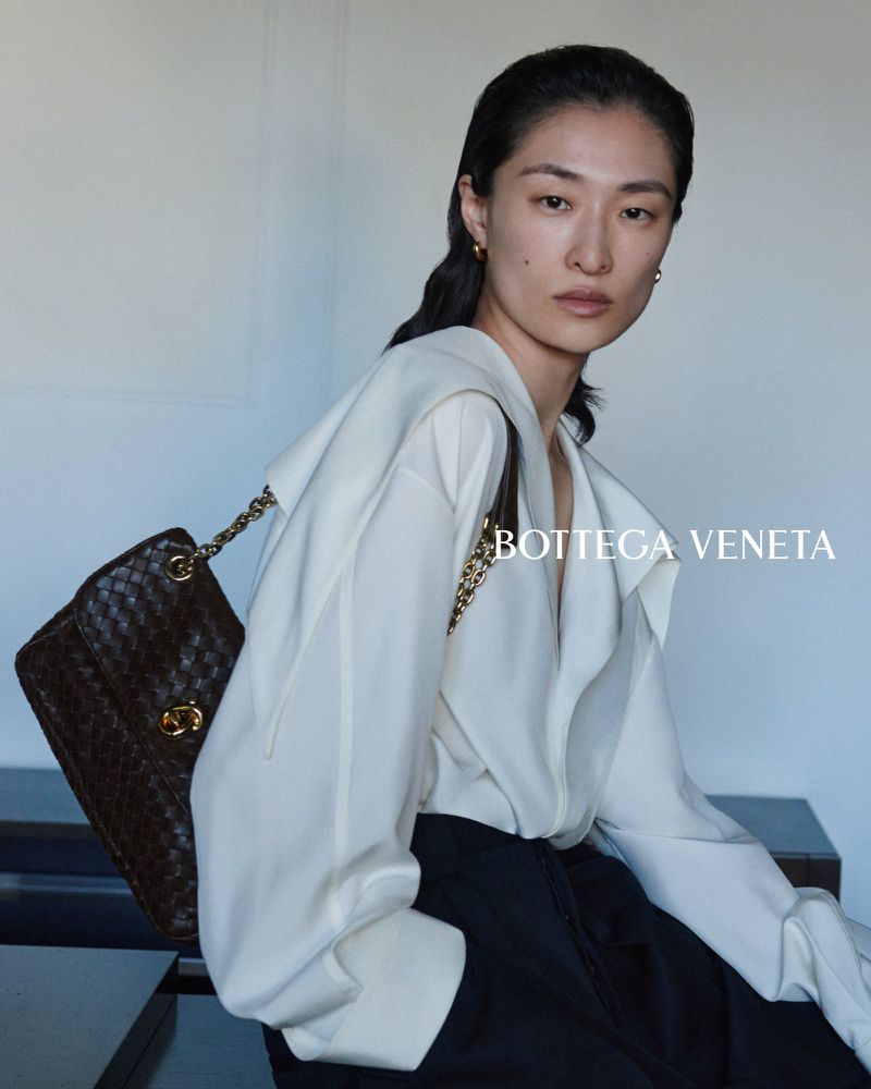 Model Chu Wong wearing an off-white blouse and holding a woven brown leather shoulder bag for Bottega Veneta