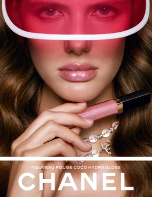 Model wearing a translucent pink visor and holding a tube of Chanel Rouge Coco Hydra Gloss to her lips.