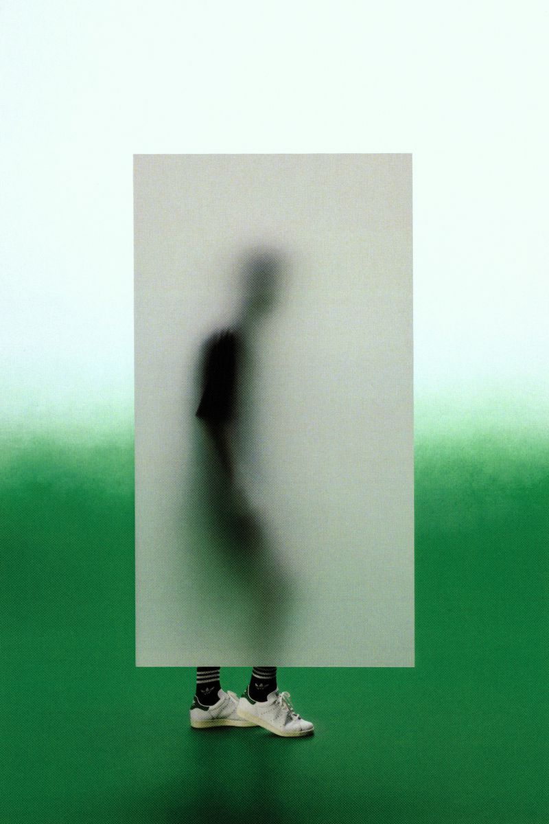Silhouette of a person walking behind a frosted screen wearing white sneakers and black socks on a green floor.