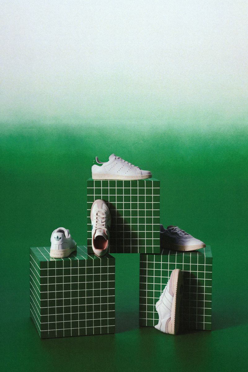 White leather sneakers arranged on green grid-tiled cubes against a green gradient background.