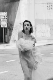 A woman wearing a sheer off-the-shoulder ruffled dress posing in black and white on an urban street.