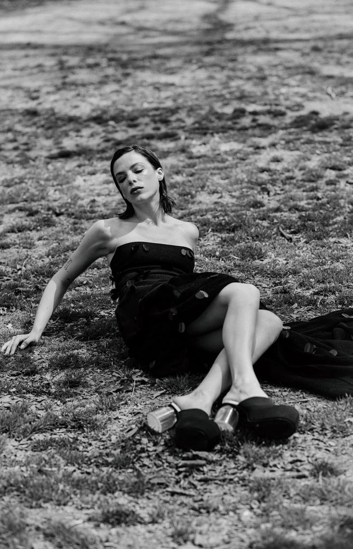 Monochrome fashion portrait of a woman reclining on grassy ground in a strapless black dress and platform mules.