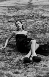 Monochrome fashion portrait of a woman reclining on grassy ground in a strapless black dress and platform mules.
