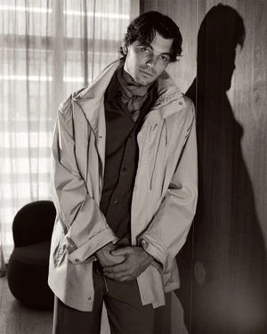 Taylor Fritz wearing a light jacket and scarf leaning against a wall in a monochromatic editorial portrait for GQ Australia