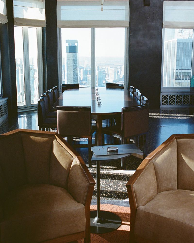 High-rise conference room with tan armchairs in the foreground and a boardroom table overlooking a sunlit city skyline.