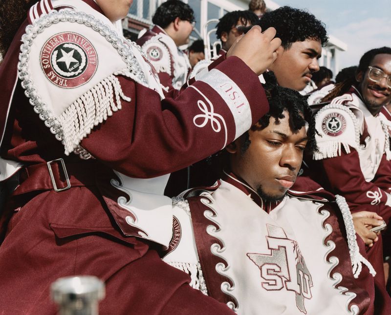 Marching band members wearing maroon and white uniforms with Texas Southern University insignias outdoors.