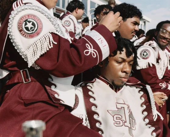 Marching band members wearing maroon and white uniforms with Texas Southern University insignias outdoors.