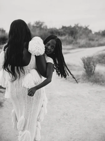 Black and white portrait of a woman carrying a child on her back along an outdoor path for American Vogue.