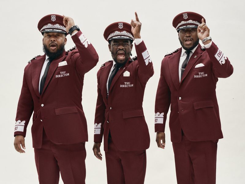 Three Black men in matching maroon peaked caps and band director uniform suits posing against a plain white studio backdrop.