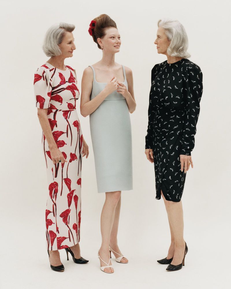 Three female models standing together against a plain white background wearing elegant dresses and high heels